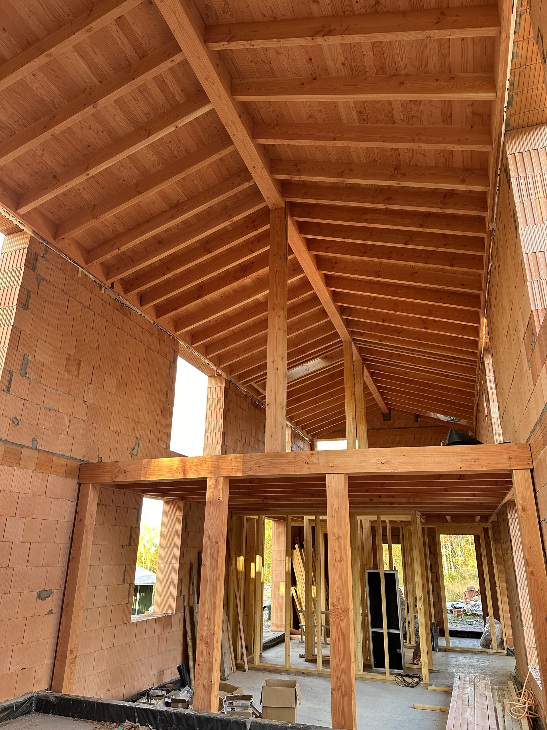 Partially constructed eco-building with exposed wooden beams, support columns, unfinished brick walls, and open framework visible inside.